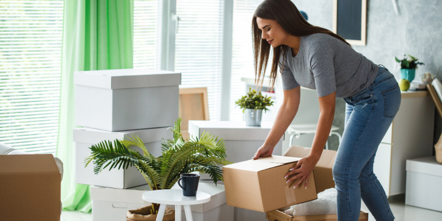 Photo of a woman moving in boxes to a living room.
